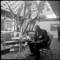 Man reading a newspaper at a cafe table, (Santa Monica?), 1950-1965