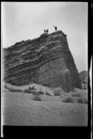 Three people wave from the top of a cliff in Red Rock Canyon State Park, California, circa 1920-1930