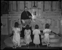 Four girls kneel before an altar as Bishop John J. Cantwell holds a Crucifix, Los Angeles, 1920-1939