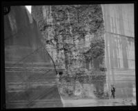 Man standing next to the remaining center portion of the Saint Francis Dam after the failure of the Dam, San Francisquito Canyon (Calif.), 1928