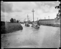 Line of automobiles driving down a rain-flooded street, Compton, [1930-1939?]