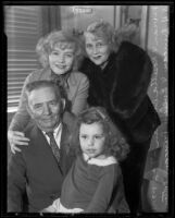 Actresses and sisters Rosetta Duncan and Vivian Duncan stand behind their father who holds his granddaughter, Evelyn, on his lap, Los Angeles, 1935