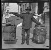 Chinese man carrying 2 baskets suspended from a yoke resting on his shoulder in Chinatown, San Francisco, 1903