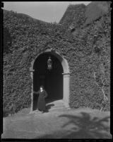 Woman stands beneath the archway of a vine-covered mansion, Los Angeles vicinity, 1936