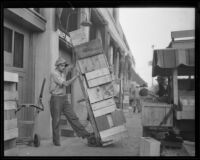 Man with a stack of crates at a produce market, Los Angeles, 1936