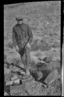 Man stands beside petrified tree remains in a dessert, California, 1920-1940