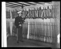 Navy officer holds a gun in a gun storage area during a militia training event, 1935