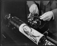 Technician manipulating a component on a Wirephoto machine with photographic print wrapped around its cylinder, Los Angeles, 1935