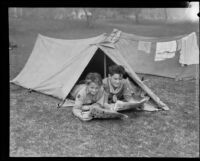 Boy Scouts read newspapers in a pup tent at a camping event in a park, circa 1935
