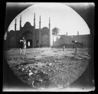 Imamzadeh-ye Hossein shrine entrance view with a man on a donkey and William Sachtleben's bicycle in the foreground, Qazvīn, Iran, 1891