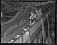 Fiancés Ann McNaughten and Hal Booth laugh with Ann’s parents, Mr. and Mrs. McNaughten while going down a slide, Los Angeles, 1936