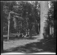 Two people stand by a tent and pile of supplies in a temporary campground, Yosemite National Park, about 1929