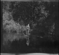 H. H. West Jr. holds a paddle and stands on a raft in a stream, Yosemite National Park, about 1929