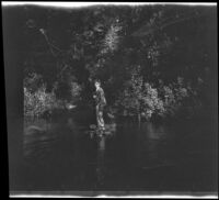 H. H. West Jr. holds a paddle and stands on a raft in a stream, Yosemite National Park, about 1929