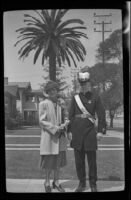 Mertie West and H. H. West, in Knights Templar uniform, pose with a large palm tree in the background, Los Angeles, 1939