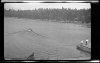 Three people on a boat landing watch people in a canoe on Lake Arrowhead, circa 1923