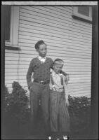 H. H. West Jr. stands next to the West's house with his arm around a boy, Los Angeles, about 1932