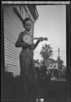 H. H. West Jr. stands next to the West's house holding a banjo, Los Angeles, about 1932