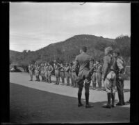 Scoutmaster, Ed Saxton, with his back to the camera, stands with Boy Scouts who are lined up at Camp Arthur Letts, Los Angeles, 1933
