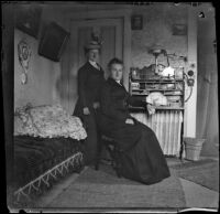 Edith Parsons stands as Nella Brydolf sits on a chair at a desk, Burlington, 1900