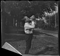 Walter Biddick drinks a soda standing on a front lawn, Burlington, 1900