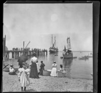 People stand on the beach and pier, while boats come to shore, Santa Catalina Island, about 1901