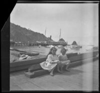 Elizabeth and Frances West sit on a pile of wood on a dock, Santa Catalina Island, about 1910