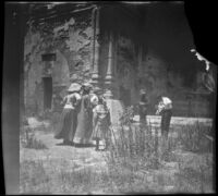 Three women and a girl stand in the transept of the ruins at San Juan Capistrano Mission and look towards the choir, San Juan Capistrano, about 1912