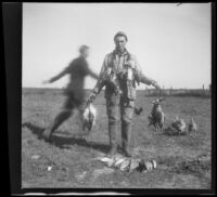 Charlie Stavnow poses with ducks killed on a shoot as a man runs behind him, Orange County vicinity, about 1912