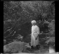 Minnie West stands near a creek, Mammoth Lakes vicinity, 1915