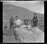 Wilfrid Cline, Glen Velzy and Charles Stavnow eat supper on a rock by the road, Lone Pine vicinity, 1918