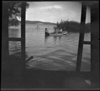 Three men sit in a boat on a flooded Crane Lake, Gorman vicinity, circa 1910s