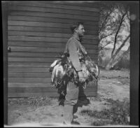 Roger Stearns stands in profile and poses with ducks outside the clubhouse, Gorman vicinity, circa 1910s