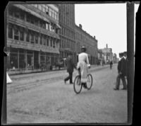 Woman rides a bicycle as men cross the street in front of her, Denver, 1900