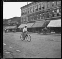 Woman rides a bicycle down a street, Denver, 1900