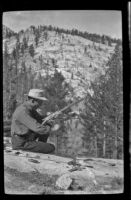 Cleo Swain on a log near the camp near Gardner Creek trying out his rifle, about 1919