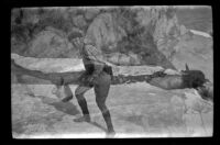 Jesse Brown climbs up a snowbank and H. H. West poses with fish, June Lake, about 1920