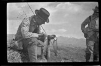 Charlie Stavnow sits and holds 2 trout caught in Convict Creek, Mammoth Lakes vicinity, about 1920