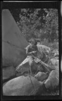 H. H. West, Jr. sits among rocks and boulders with his fishing gear, Ojai vicinity, about 1925