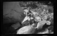 H. H. West, Jr. sits on a rock and tends to his fishing gear, Ojai vicinity, about 1925