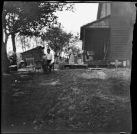 H. H. West sits in a backyard churning butter, Elliott vicinity, 1900