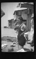 Mertie West kneels in the sand at the Morgan's beach cabin while Josie Shaw peeks behind her, Malibu, about 1930