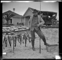 H. H. West posing on the beach with several fish and his fishing rod, Newport Beach, 1914