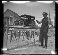 Glen Velzy standing on the beach with fish he caught, Newport Beach, 1914