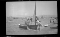 People meddling with a dinghy on the shore, Newport Beach, 1938
