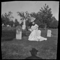 Ellen Lorene (Pinkie) Lemberger kneels next to a headstone holding a bouquet of flowers, Ottumwa, 1900