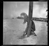 Mary Whitaker standing behind a post and tossing sand at the camera, Redondo Beach, 1901