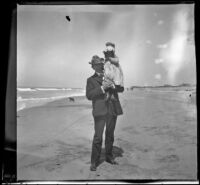 H. H. West posing on the beach with a toddler, Redondo Beach, 1901