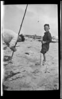 H. H. West, Jr. posing while an unknown man tends to a fishing rod at Rincon Point, Carpinteria vicinity, about 1924