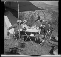 Group sits at a table at their campsite near Rush Creek, Mono County vicinity, 1929
